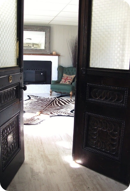 Svarte dører åpne med utsikt til stue med sebraskinn foran grønn lenestol.